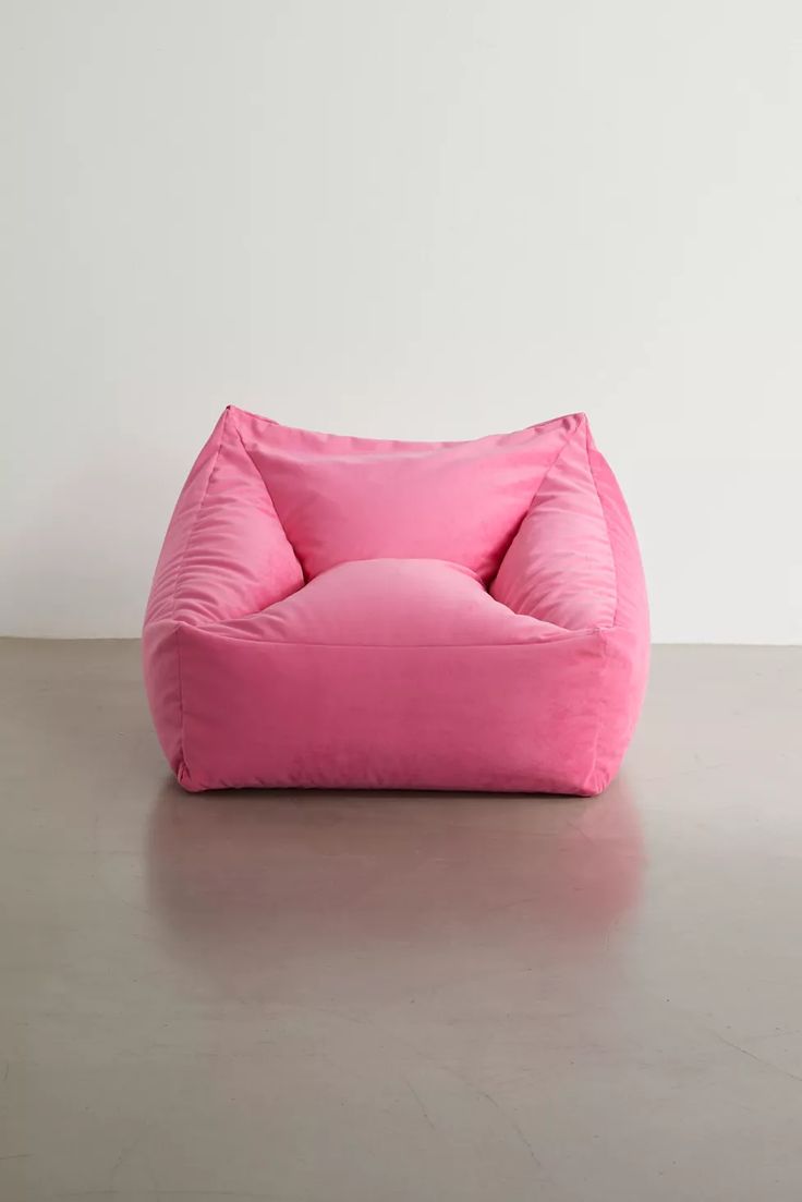 a pink bean bag chair sitting on top of a cement floor next to a white wall