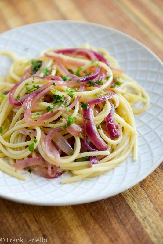 a white plate topped with pasta and veggies on top of a wooden table