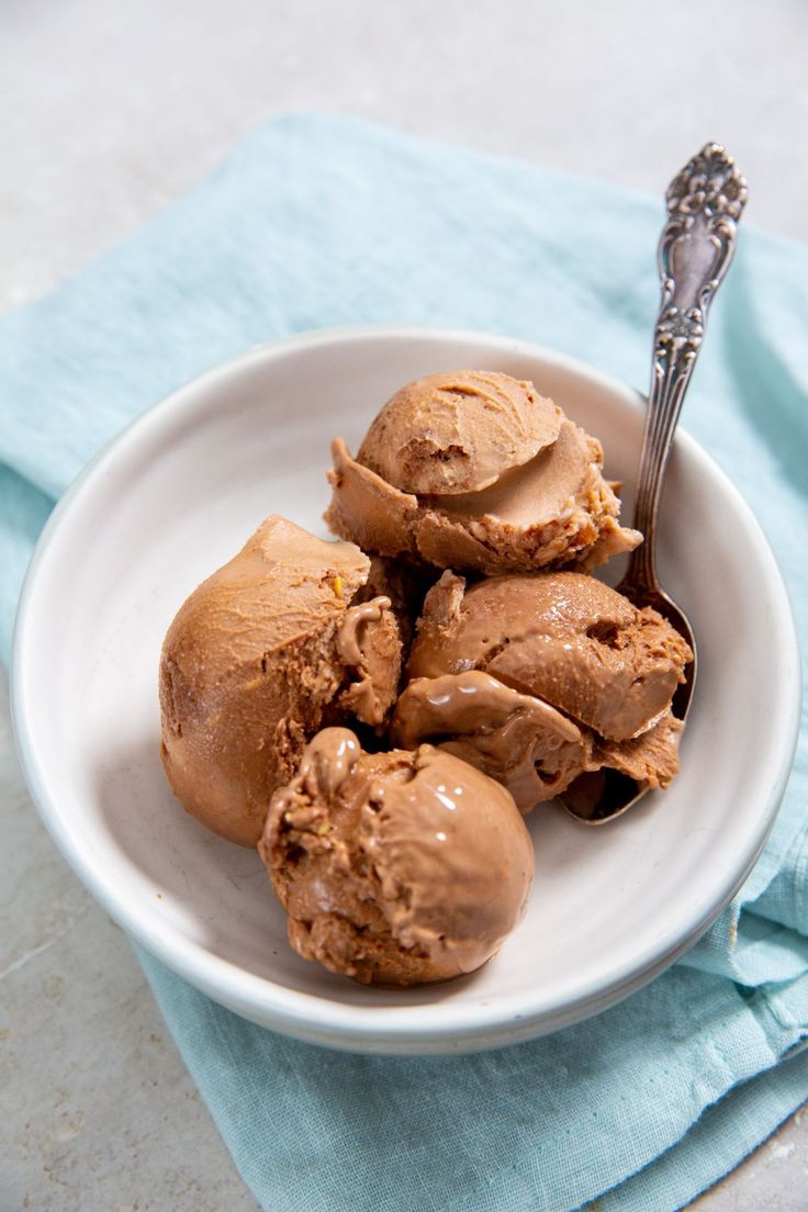 three scoops of ice cream in a white bowl on a blue napkin with a spoon