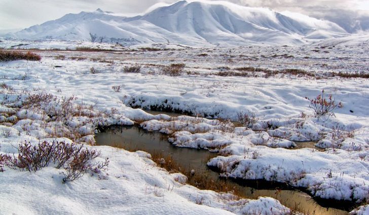 a snowy landscape with mountains and water in the foreground, snow on the ground