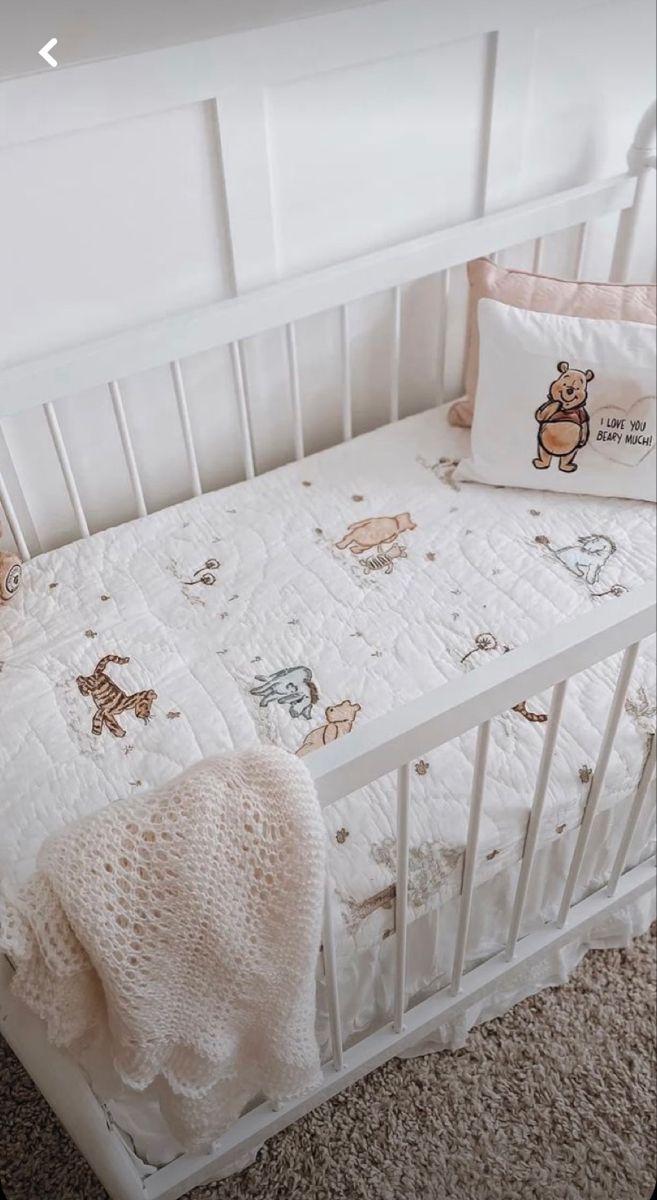 a white crib with a teddy bear blanket and pillows on it's side