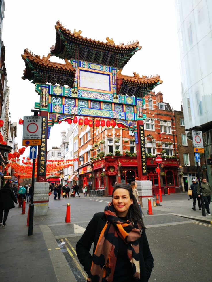 a woman standing in front of a chinese arch on a city street with red and blue decorations