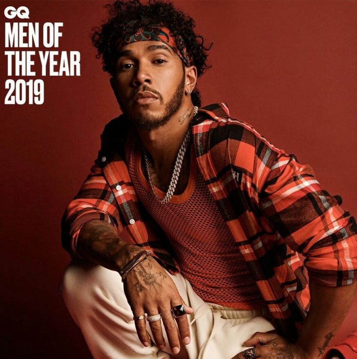 a man sitting on top of a chair wearing a red shirt and white pants with the words men of the year in front of him