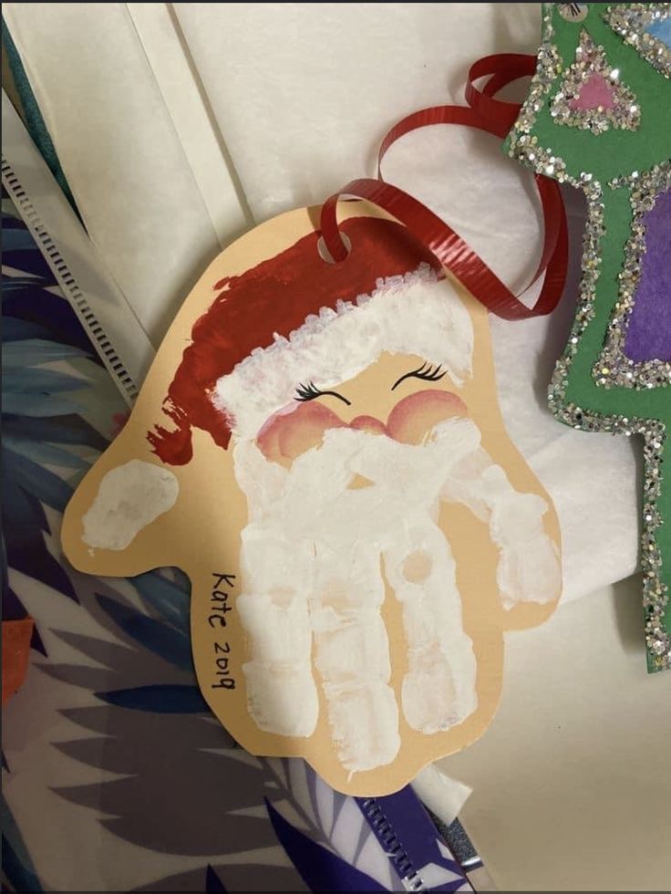 a handprinted santa clause ornament next to a christmas tree ornament