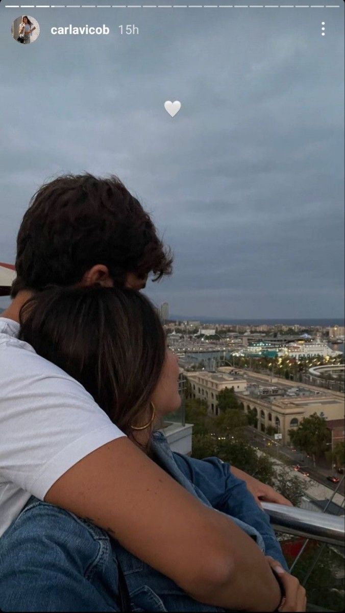 a man and woman sitting on top of a balcony looking at the city below them