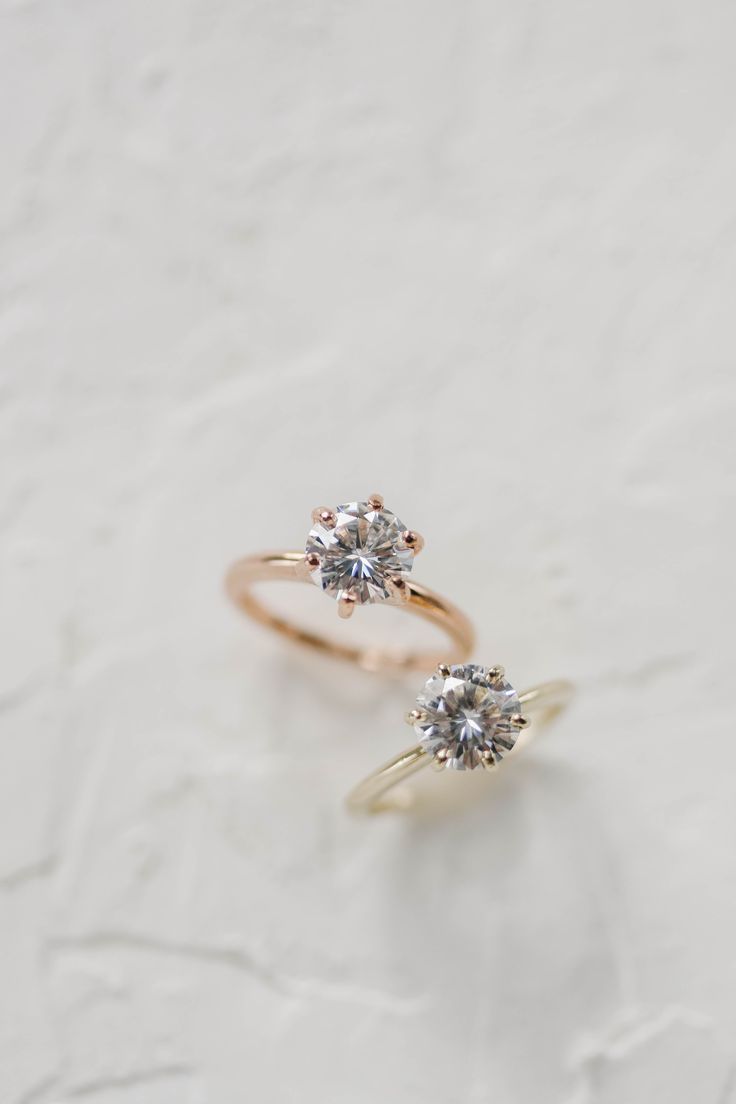 two gold rings with diamonds on them sitting on a white surface in front of the camera