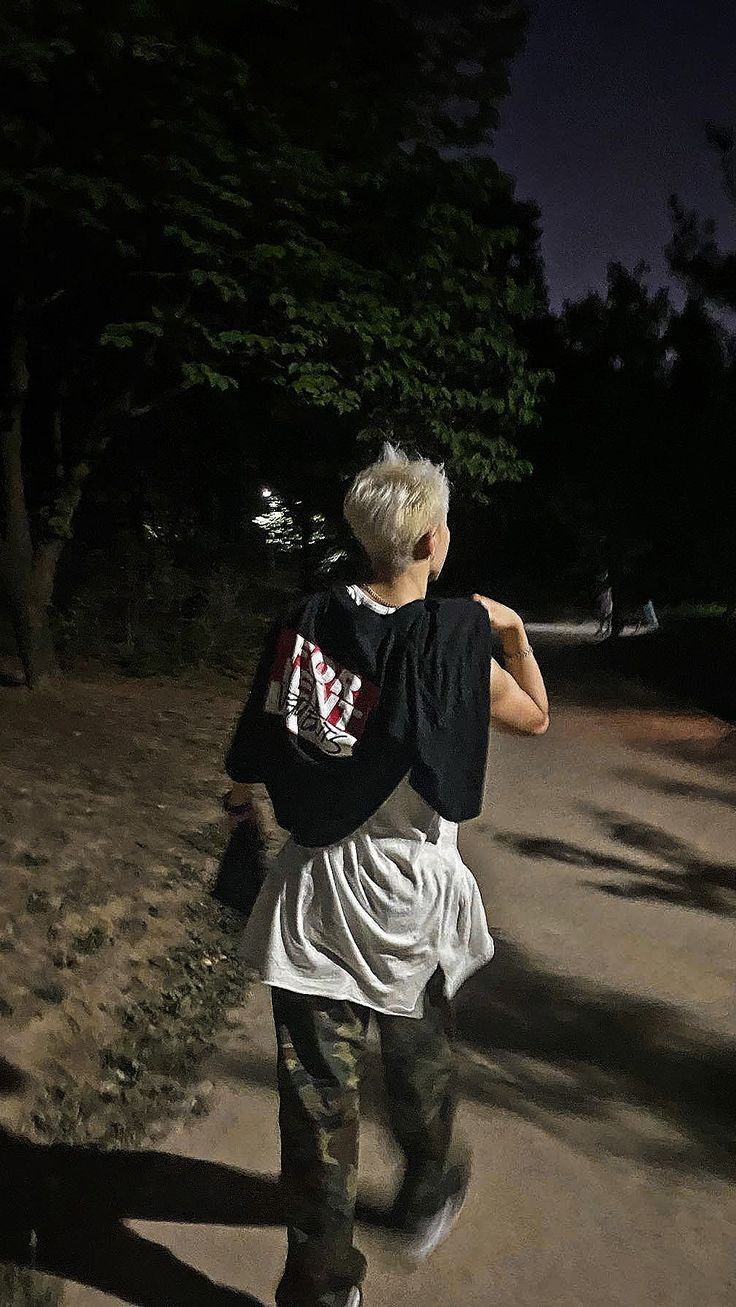 a man walking down a dirt road at night with his back turned to the camera