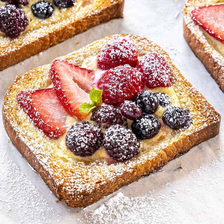 several pieces of bread with berries and powdered sugar on top, sitting on a table