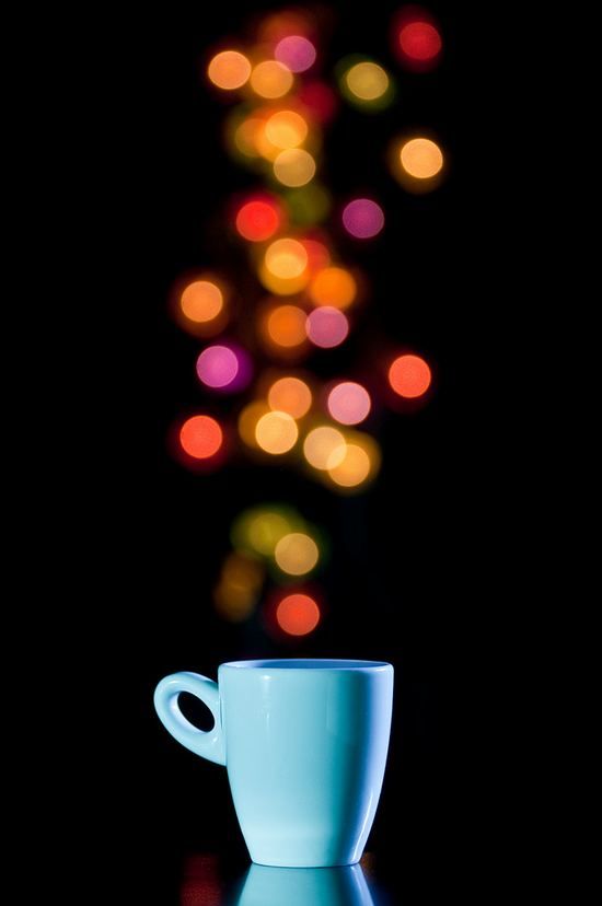 a blue coffee cup sitting on top of a table next to a lit up christmas tree