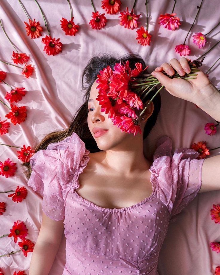 a woman laying on top of a pink bed covered in flowers and holding her head