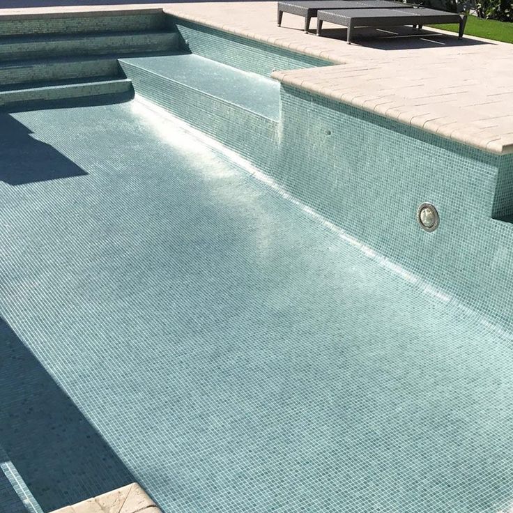 an empty swimming pool with steps leading up to the edge and benches in the background