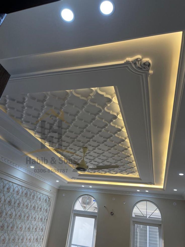 the ceiling in this room is decorated with white and gold decorations, along with two large windows