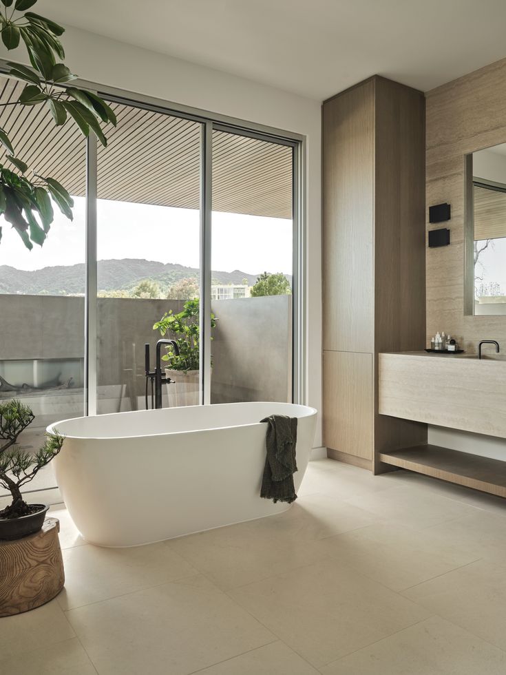 a bathroom with large windows and a white bathtub next to a potted plant