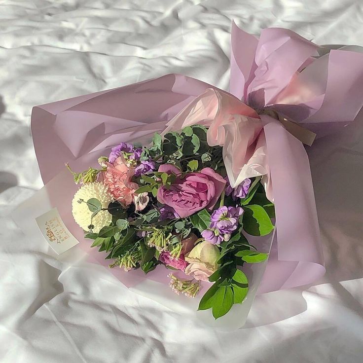 a bouquet of flowers is wrapped in pink paper on a bed sheet with white sheets