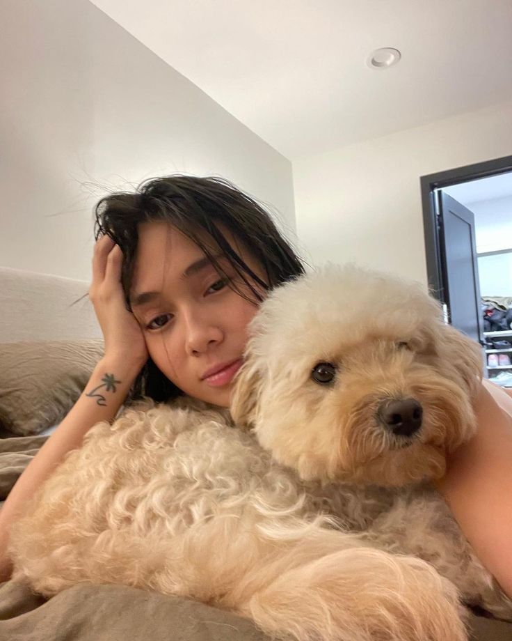 a woman laying on top of a bed holding a dog