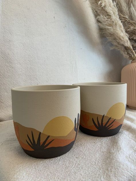 two cups sitting on top of a bed next to a vase with plants in it