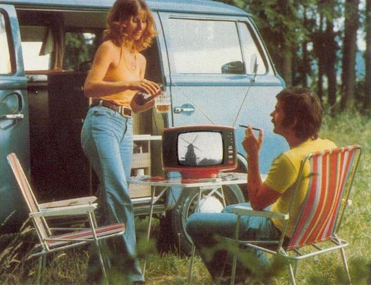 a man and woman sitting in lawn chairs next to an old vw camper van