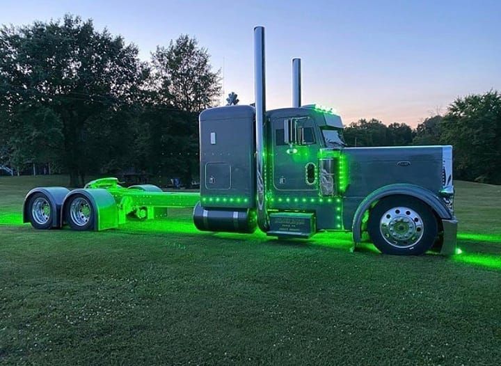 a large semi truck parked on top of a lush green field with trees in the background