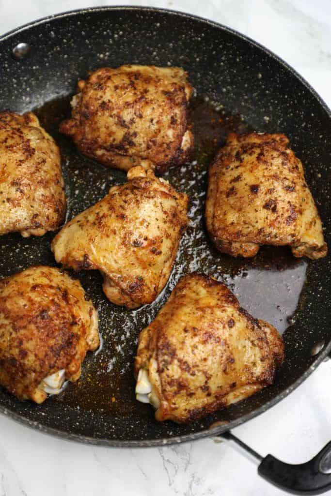 chicken thighs cooking in a skillet on a stove top with oil and seasoning