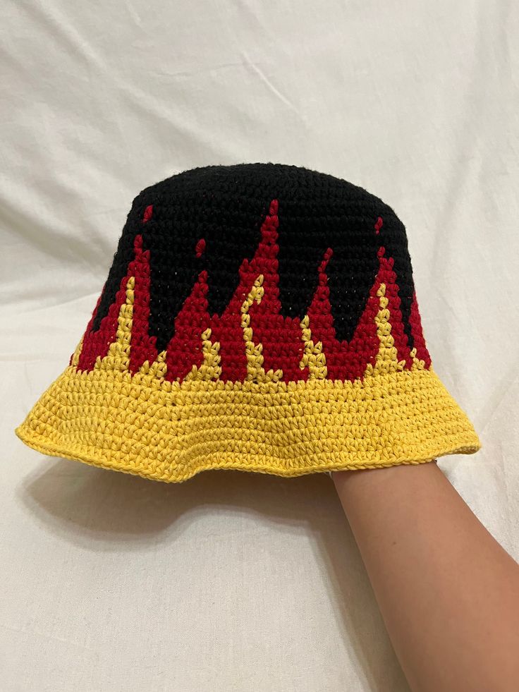 a crocheted hat with flames on it is being held up by someone's hand