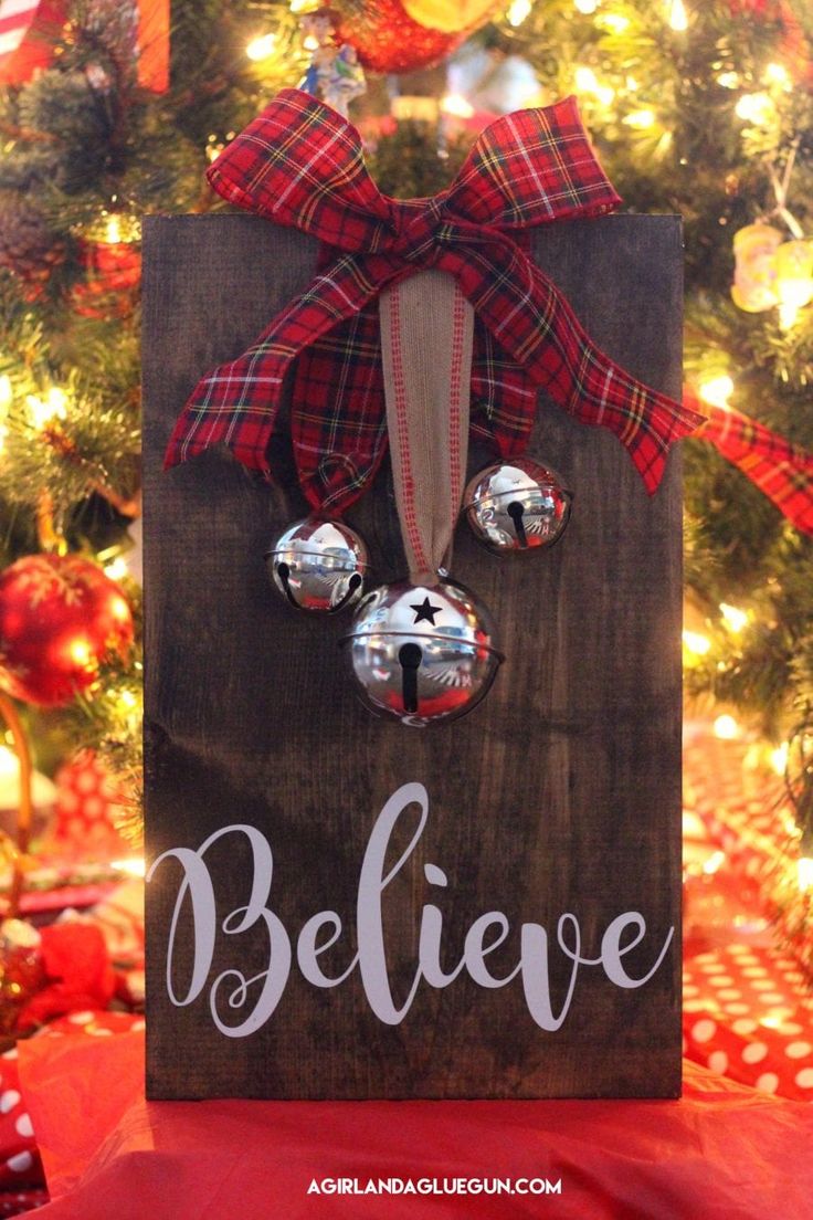 a christmas ornament hanging on a wooden sign that says believe with bells in front of a christmas tree