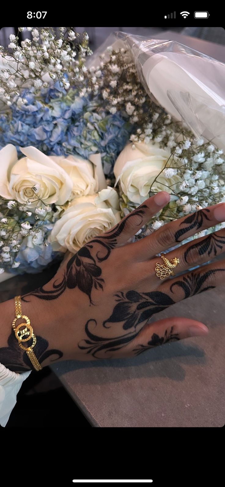 a woman's hand with tattoos on it and flowers in the backgroud