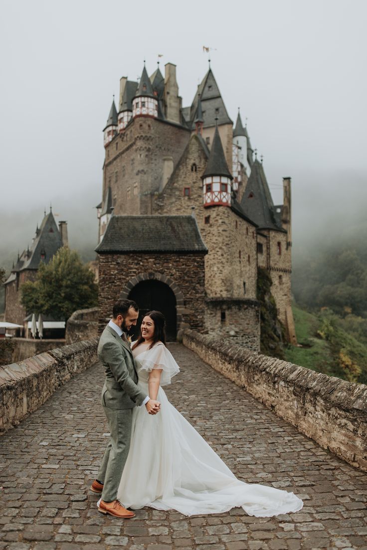 a bride and groom standing in front of an old castle on a foggy day