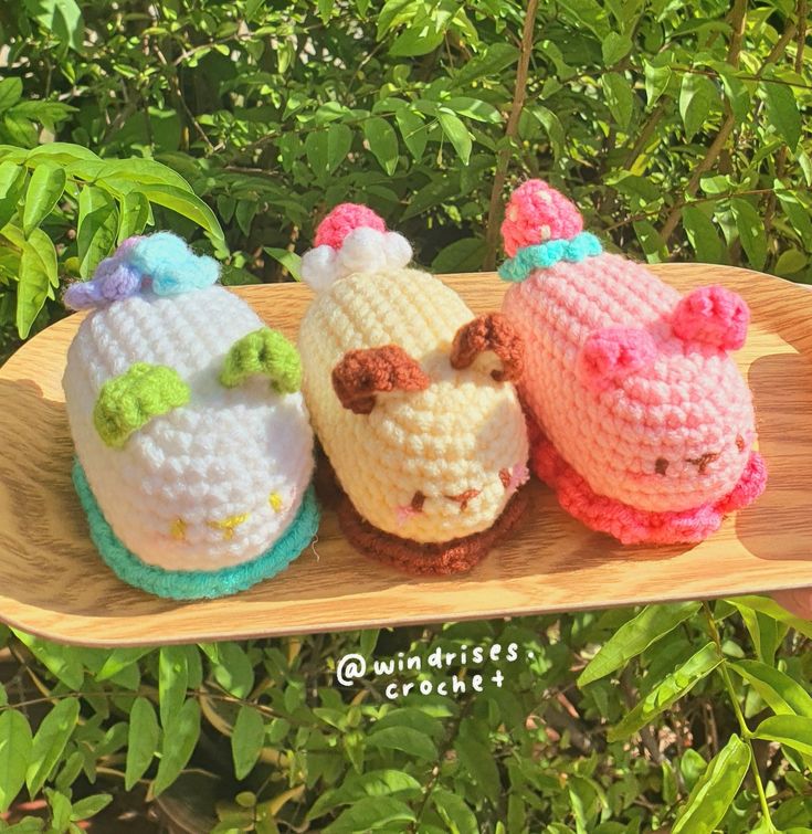 three small crocheted cakes sitting on top of a wooden tray next to green leaves