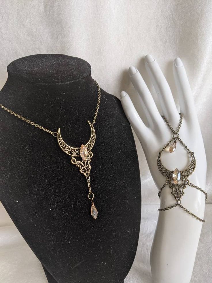 A beautiful and unique jewelry set which includes a pendant necklace and hand chain, featuring a filigree moon and connector charm with a crystal decorating the center of the moon and a drop crystal hanging from the pendant. Choose Crystal Shape between horse eye (as pictured) or teardrop (horse eye will be sent if unspecified) Choose necklace length from the diagram in the listing picture (14 inches plus 1.5 inch extension chain will be sent if unspecified) Elegant Moonstone Jewelry For Festivals, Crescent Moon Charm Jewelry For Parties, Crescent Moon Charm Party Jewelry, Elegant Moon Phase Jewelry For Festivals, Elegant Moon Phase Festival Jewelry, Metal Jewelry With Moon Charm For Party, Moon Charm Pendant Jewelry For Party, Bohemian Moon Charm Jewelry For Party, Party Pendant Jewelry With Moon Charm