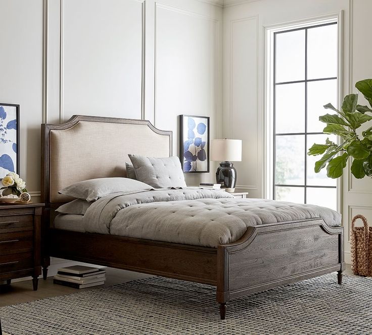 a bedroom with a bed, nightstands and plants on the floor in front of large windows