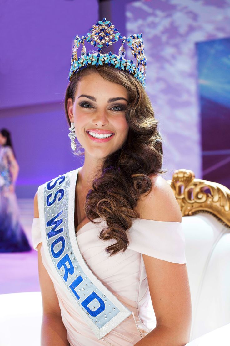 a beautiful young lady wearing a tiara and smiling at the camera while standing in front of a stage