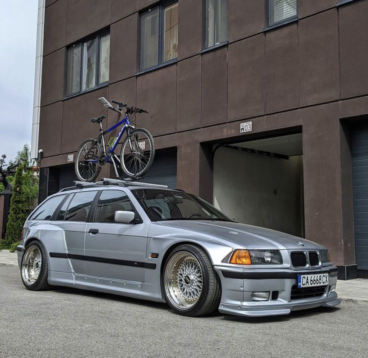 a silver car parked in front of a building with a bike on top of it