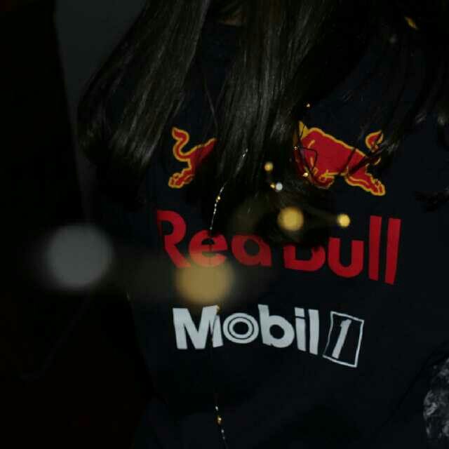 a woman wearing a red bull t - shirt holding a cell phone