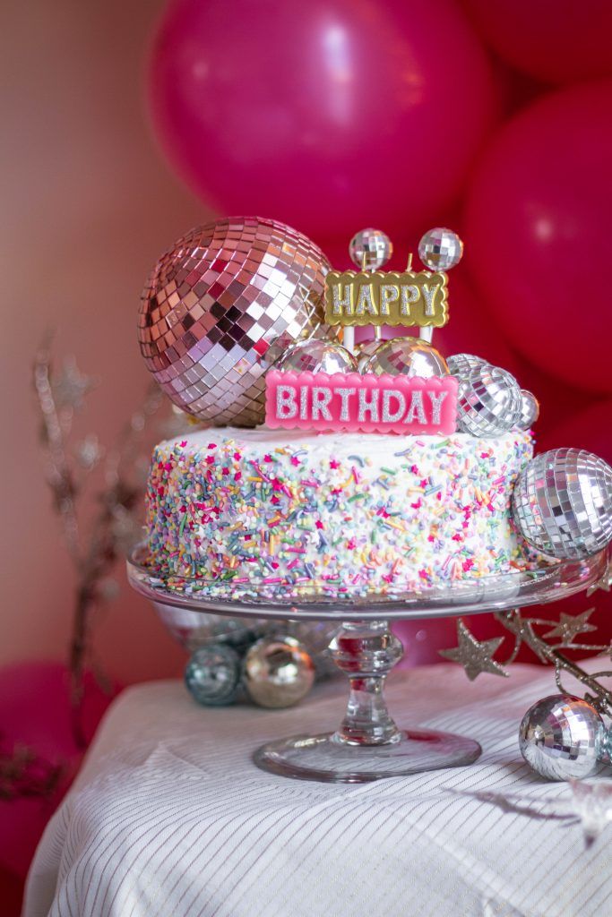 a birthday cake sitting on top of a table next to balloons and confetti