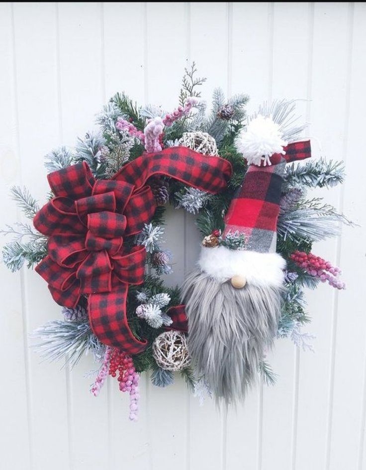 a christmas wreath with a gnome face and red plaid ribbon hanging on a white door