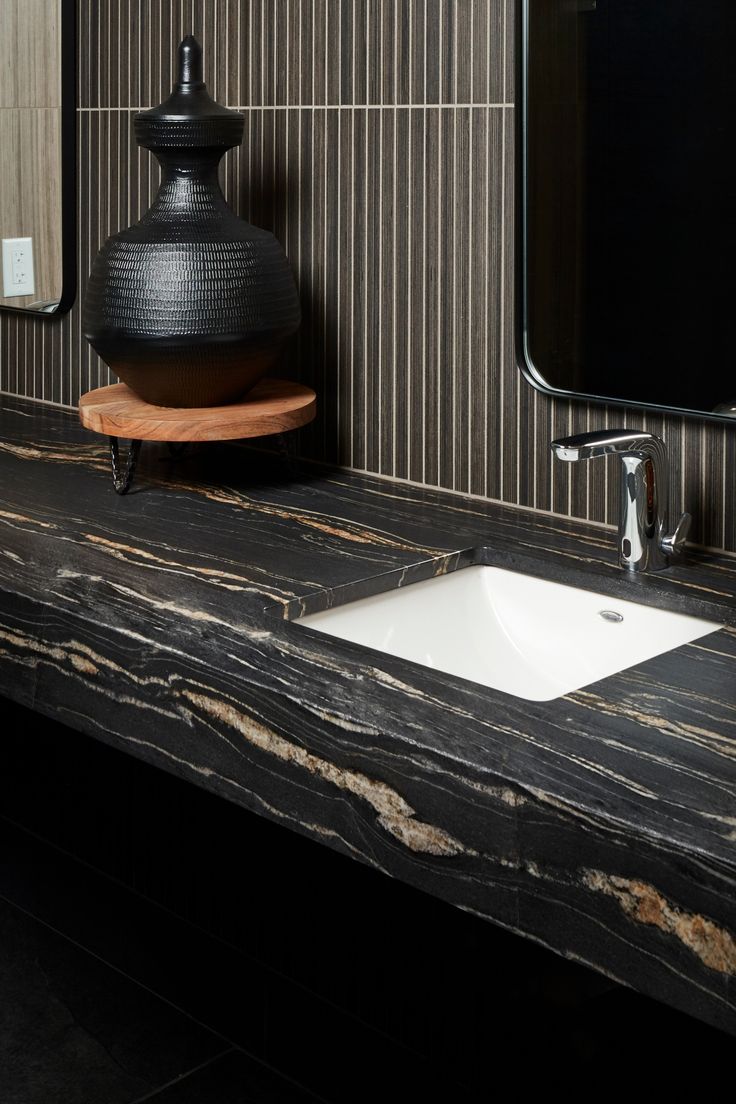 a bathroom sink sitting under a mirror next to a black vase on top of a counter