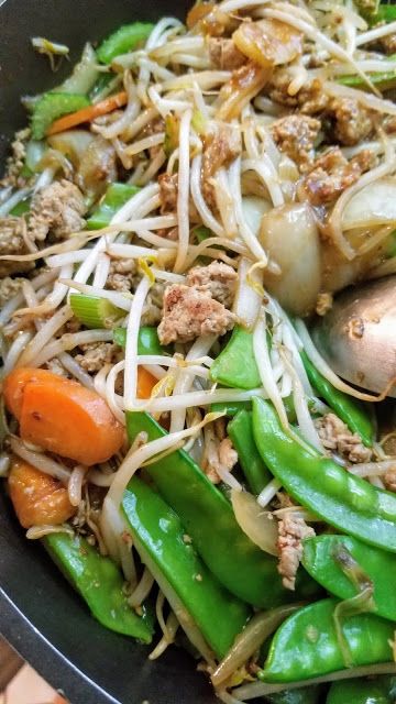 stir fry with meat, vegetables and noodles in a black bowl on a wooden table