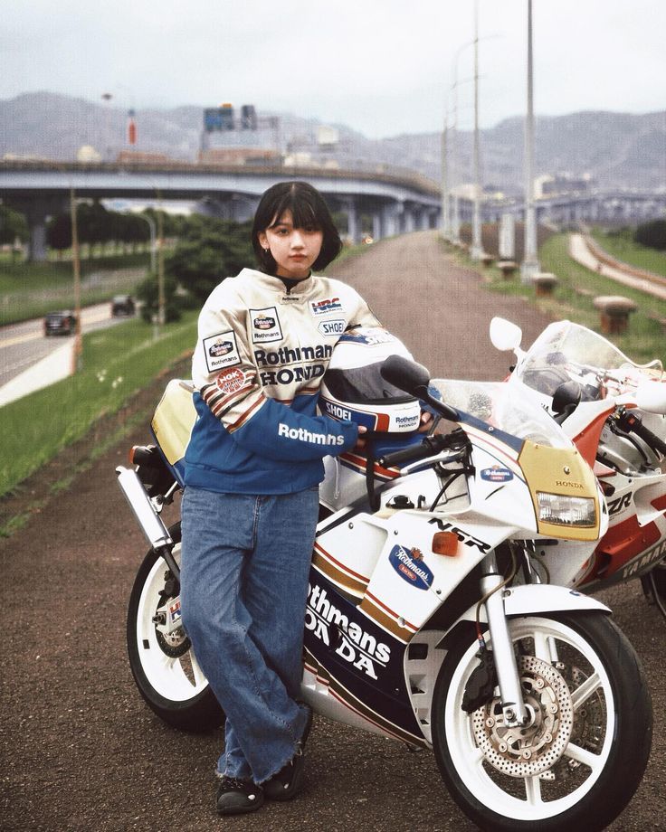 a person standing next to a motorcycle on a dirt road with mountains in the background