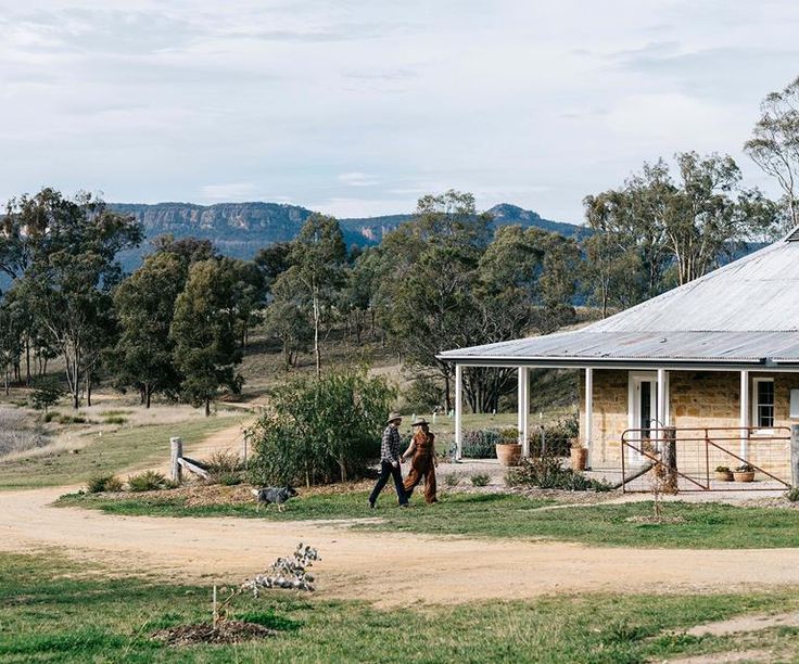 two people walking in front of a small house with mountains in the backgroud