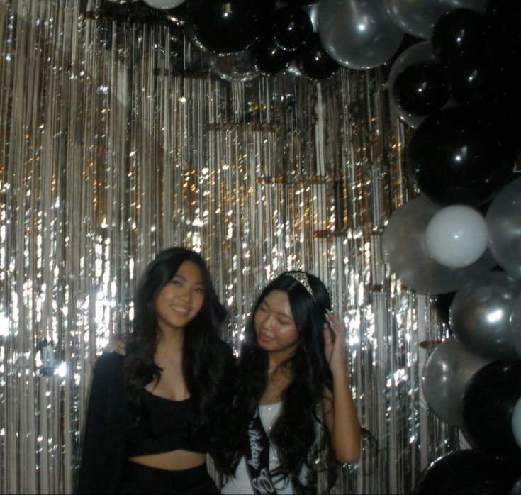 two young women standing next to each other in front of balloons and streamers on the wall