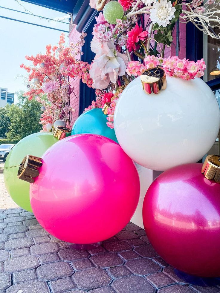 three large, colorful balls are sitting on the ground next to some pink and white flowers