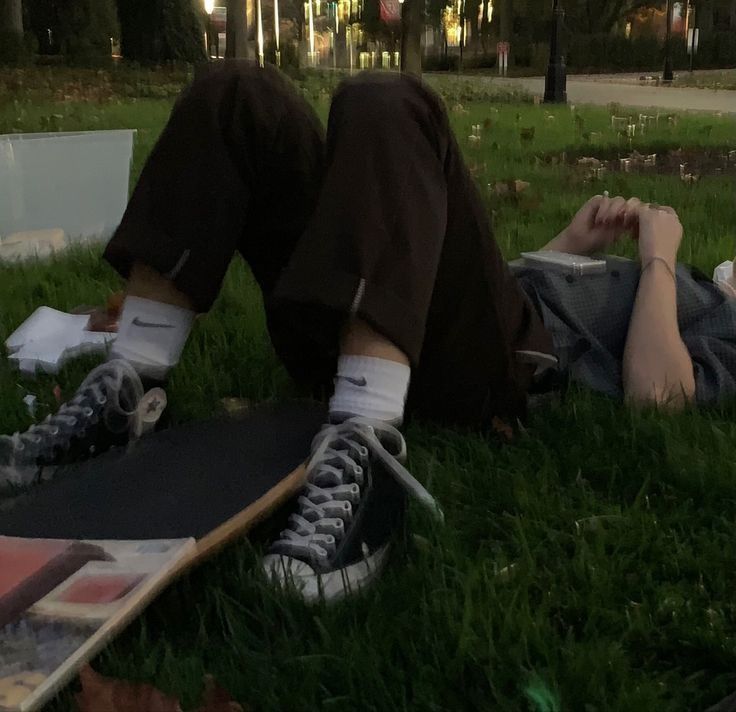 a man laying on the ground with his skateboard next to him and another person lying down in the grass