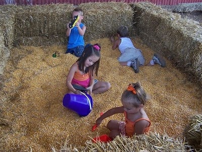 three children playing in hay with buckets and sand on the ground next to straw bales