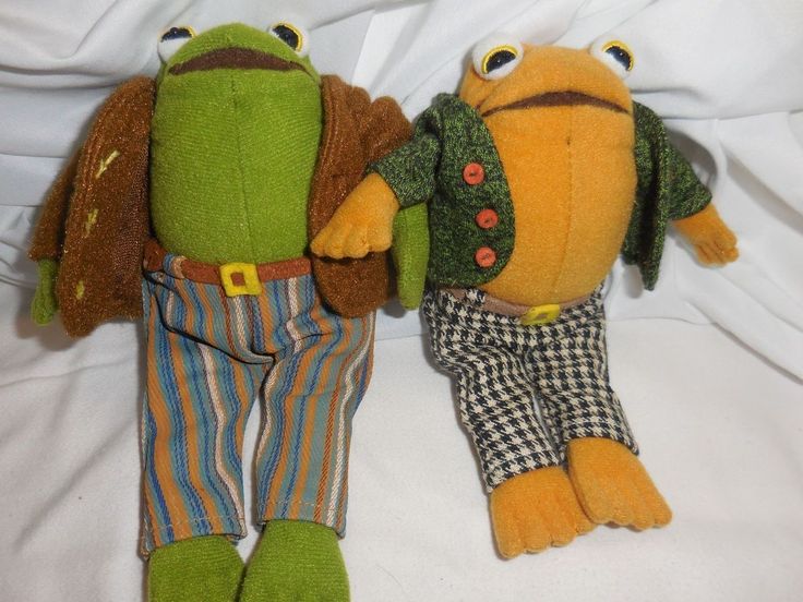 two stuffed animals sitting next to each other on a white sheet covered bed, one is green and the other is brown