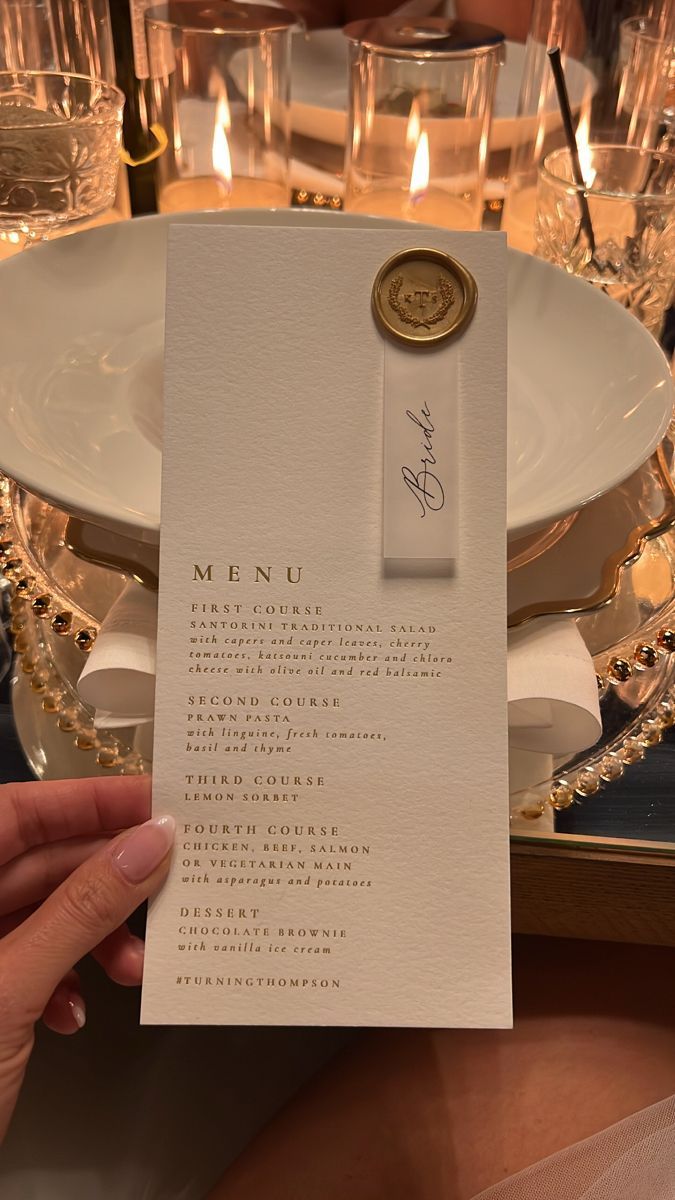 a person holding up a menu in front of a table set with glasses and candles