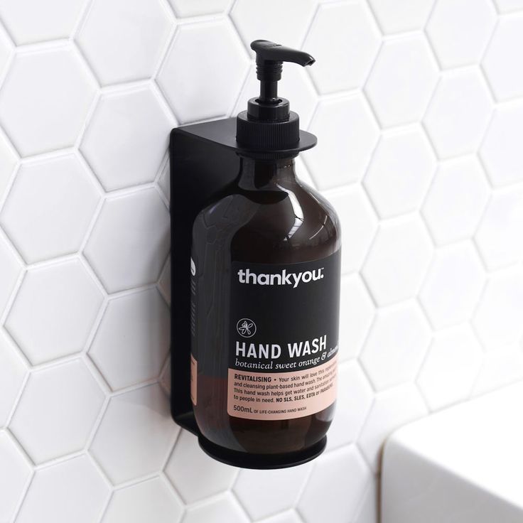 a black soap dispenser hanging on a white tiled wall