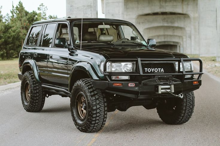 a black toyota truck is parked on the side of the road in front of an overpass