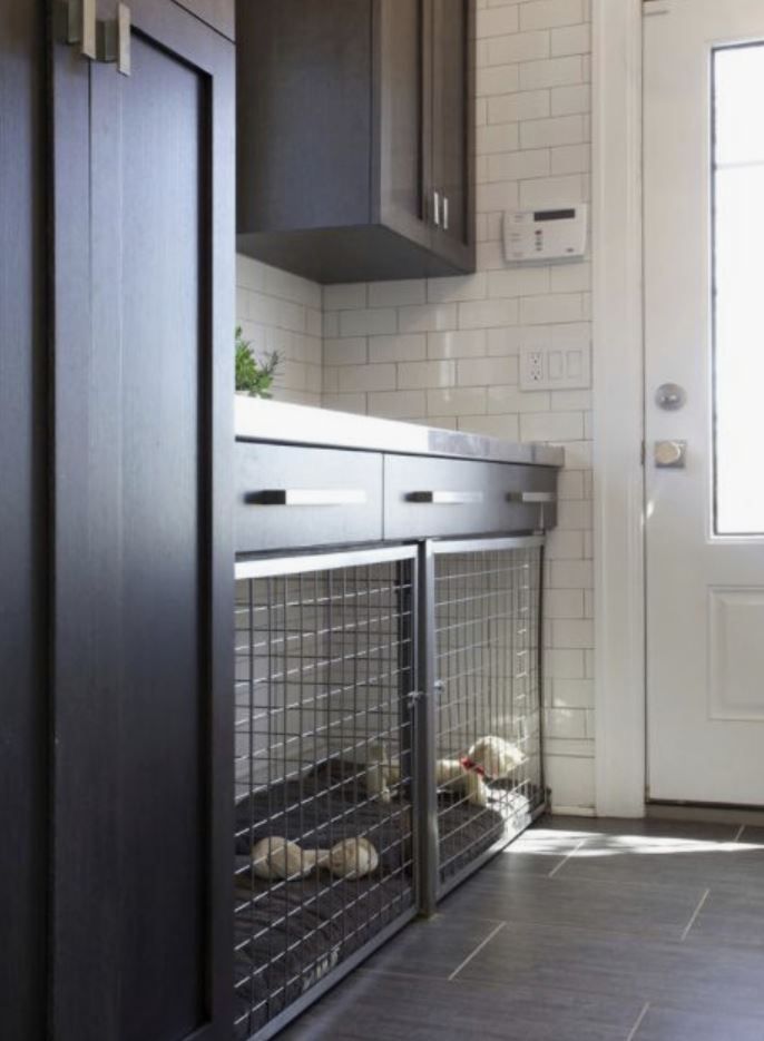 a dog is in its kennel at the entrance to his home, which has white brick walls and dark wood cabinets