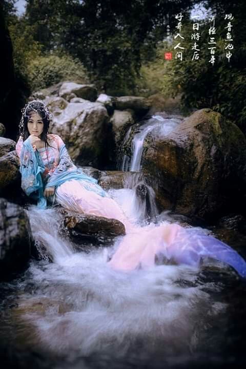 a woman sitting on top of a rock next to a river filled with rocks and water