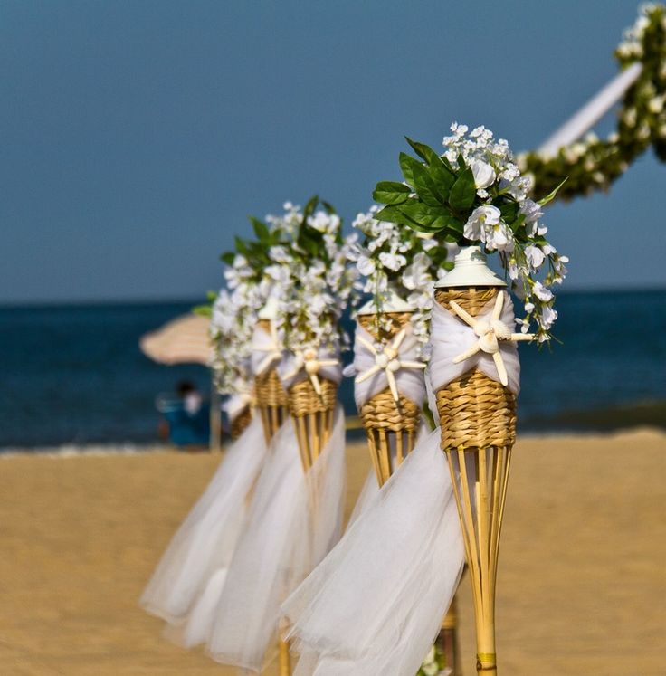 wedding decorations on the beach with flowers in baskets and ribbons tied to them, along with an umbrella